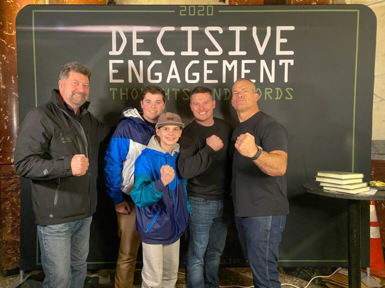 Ryan Lucas and family meeting Jocko Willink and flexing in front a background that reads "2020 Decisive Engagement"