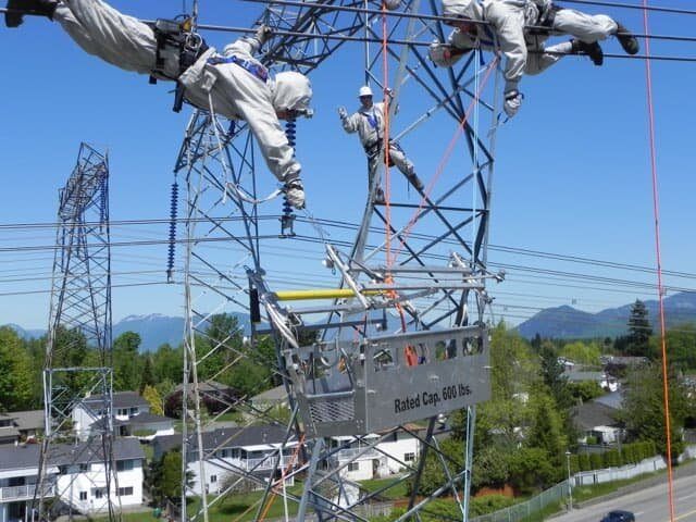 Three lineman workers dangling and working on transmission lines.